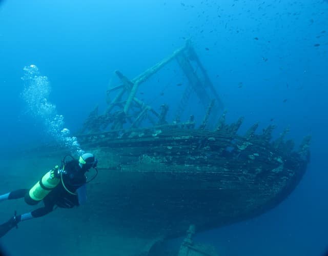 Scuba diver exploring a historic shipwreck underwater during an advanced open water wreck diving adventure